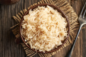 Bowl of shredded cabbage (sauerkraut) on a wooden table with a fork nearby.