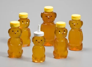 Assorted honey bear bottles with yellow caps arranged on a light surface.